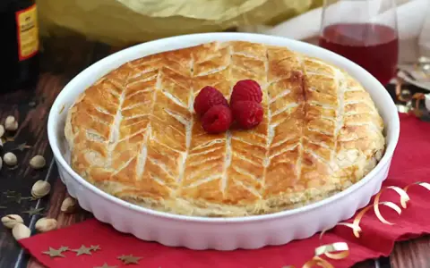 Une délicieuse galette pistache framboise dorée, décorée de fruits rouges frais, prête à être dégustée.
