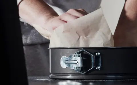 Mains expertes s'affairent à chemiser un moule avec du papier sulfurisé, préparant ainsi le terrain pour une future création culinaire.