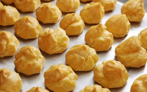 Une fournée de choux à la crème dorés, prêts pour la cuisson. Ils attendent patiemment d'être transformés en délices.