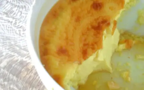 Un flan aux œufs à l'ancienne, doré et crémeux, servi dans un plat blanc sur une nappe texturée.