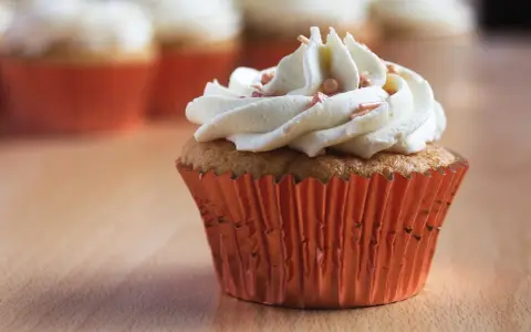 Un cupcake orné d'une généreuse ganache chocolat blanc, parsemé de perles rosées, dans un élégant caissette orange.