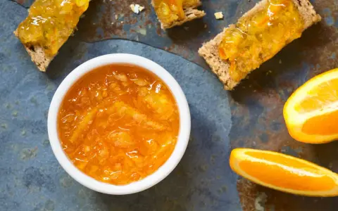 Confiture d'écorce d'orange brillante dans un bol blanc, servie sur des toasts avec des tranches d'orange fraîche.