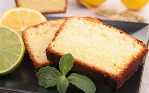 Tranches de cake au citron facile, garnies de menthe fraîche, avec des citrons et citrons verts en arrière-plan.