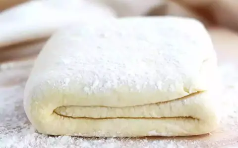 Pâte feuilletée prête à être utilisée pour votre recette. Les couches sont bien visibles, saupoudrées de farine.