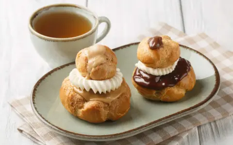 Deux religieuses au café, garnies de crème et nappées de chocolat ou de caramel, accompagnées d'une tasse de thé.