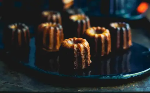 Plusieurs cannelés dorés, parfaits pour la conservation, sont disposés sur une assiette sombre.