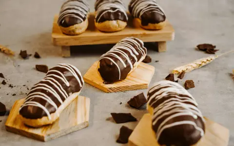 Éclairs gourmands avec un glaçage éclair chocolat brillant, décorés de fines rayures blanches. Des éclats de chocolat parsèment la table.