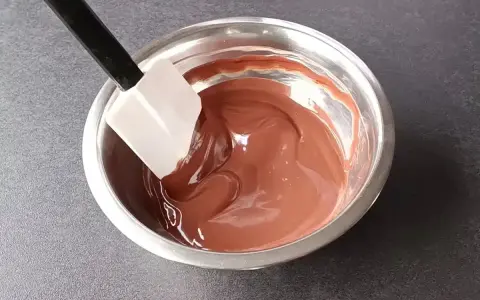 Spatule mélangeant une ganache au chocolat noir onctueuse dans un bol en métal.