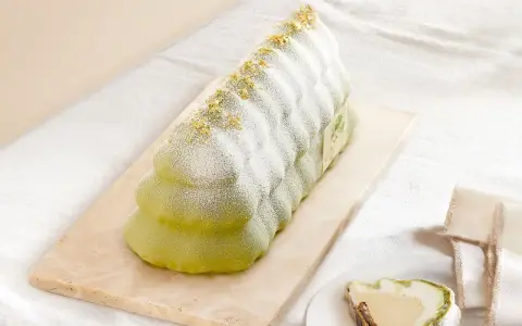 Bûche glacée verte, saupoudrée de sucre glace et de paillettes dorées, évoquant un biscuit madeleine.