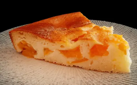 Tranche de clafoutis abricot, une création de chef, sur une assiette texturée.