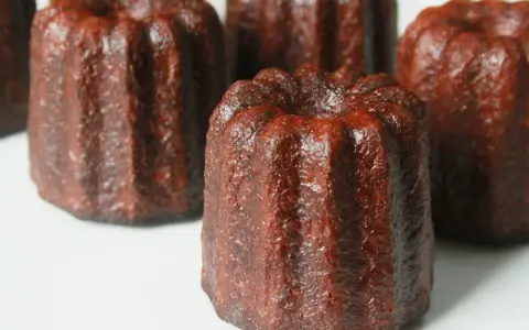 Plusieurs cannelés dorés, tout juste sortis du four, prêts pour la dégustation. La cuisson des cannelés révèle leur croûte caramélisée.
