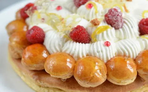 Un déliceux saint honoré framboise, orné de crème fouettée, de fruits rouges et de petites brioches caramélisées.