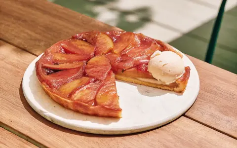 Tarte Tatin caramélisée, une part coupée, servie avec une boule de glace à la vanille. La cuisson parfaite révèle des pommes dorées et une pâte croustillante.