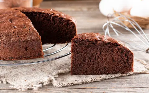 Un délicieux gâteau génoise chocolat, moelleux et aéré, prêt à être dégusté. Des ingrédients frais comme des œufs et du cacao sont visibles en arrière-plan.