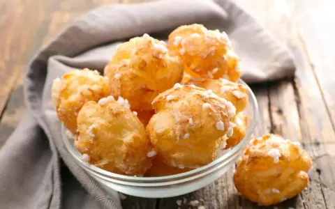 Un bol de chouquettes maison dorées et saupoudrées de sucre perlé, posé sur une table en bois.