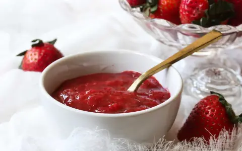 Un bol de compotée de fraise pour gâteau, prêt à être dégusté. Des fraises fraîches sont disposées autour.