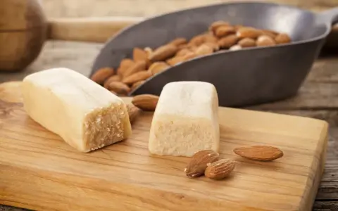 Deux blocs de pâte d'amande et des amandes dans une pelle, prêts pour une recette de pâte d'amande maison.