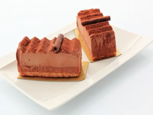Deux parts de gâteau Trianon, le meilleur pâtissier, saupoudrées de cacao, sur une assiette blanche.