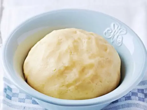 Pâte sablée prête pour la cuisson, dans un bol bleu clair. Une texture parfaite pour des tartes croustillantes.