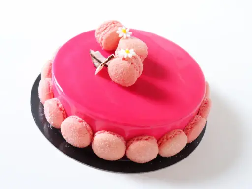 Entremet fraise rose vif, décoré de macarons roses et de petites fleurs blanches.