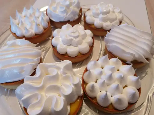 Assortiment de tartelettes garnies d'une crème citron et surmontées de **meringue italienne** aux formes variées.
