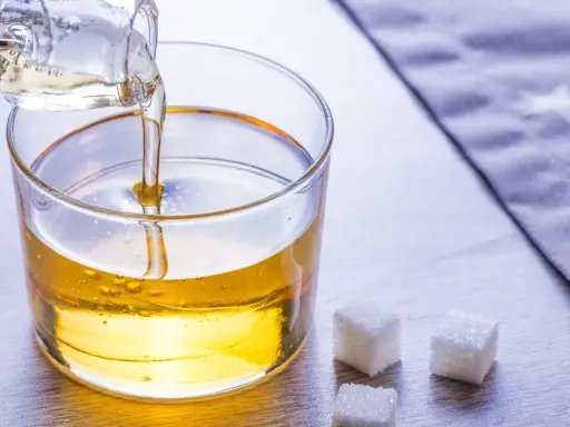 Versez le sirop de glucose dans un bol. Une recette simple pour des desserts parfaits. Trois morceaux de sucre à côté.