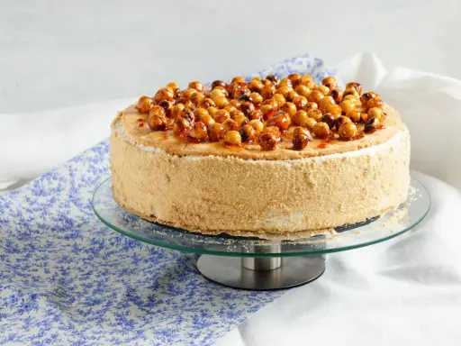 Gâteau dacquoise noisette garni de noisettes caramélisées sur un présentoir en verre.