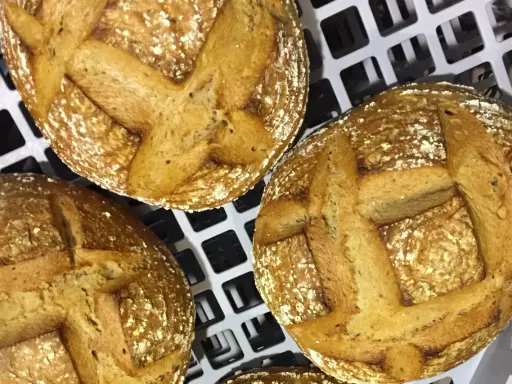 Trois pains au levain dorés, prêts pour la cuisson sur sole. Leurs croûtes craquelées et leurs incisions en croix promettent une texture parfaite.