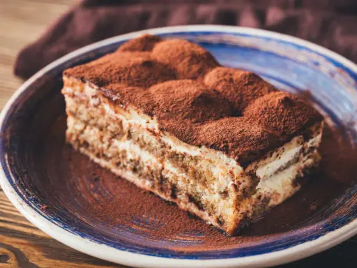 Tranche de tiramisu onctueux, saupoudrée de cacao, digne d'une recette tiramisu chef étoilé.