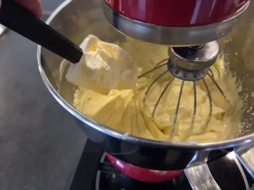 Préparation d'une crème mousseline chantilly onctueuse dans un robot pâtissier. Une spatule ajoute une touche de douceur.