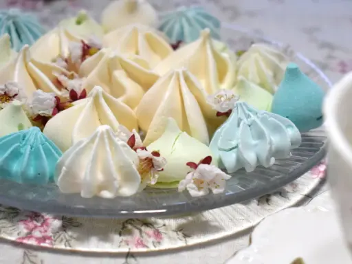 Meringues colorées, comme créées par un robot pâtissier, parsemées de fleurs délicates.