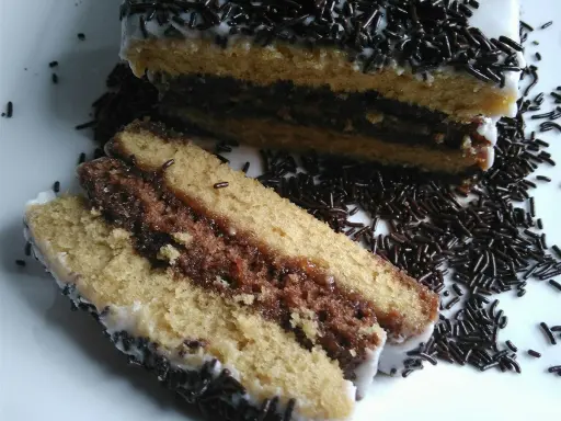 Délicieux napolitain maison, avec ses couches de génoise et de chocolat, nappé de glaçage blanc et saupoudré de vermicelles.