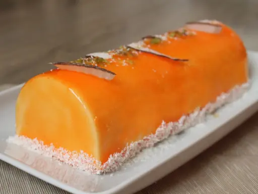 Bûche fruit exotique, un délice orangé glacé, décoré de copeaux de noix de coco et de zestes verts.