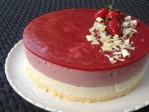 Un délicieux entremet aux trois couches, couronné d'une mousse fraise, de fraises fraîches et de copeaux de chocolat blanc. Parfait pour une occasion spéciale.