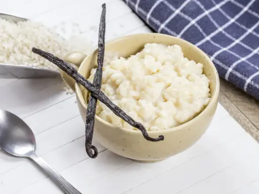 Un bol de riz au lait crémeux, garni de gousses de vanille, avec du riz brut à côté.