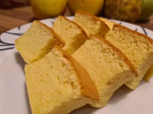 Tranches de moelleux gâteau japonais, léger et aérien, sur une assiette blanche. Des fruits jaunes sont flous en arrière-plan.