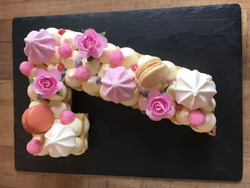 Un biscuit joconde number cake en forme de 1, décoré de crème, meringues, macarons et roses en sucre.