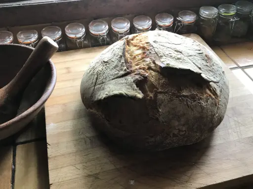 Gros pain artisanal sur une planche en bois, avec un mortier à côté. La question "peut on mélanger levain et levure" plane dans l'air.