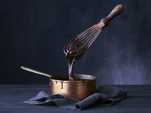 Sauce chocolat qui ne fige pas, coulante et brillante, dégouline d'un fouet dans une casserole en cuivre.