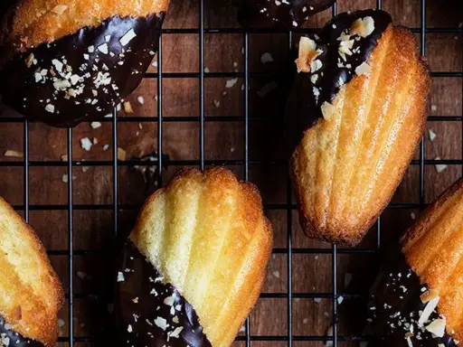 Des biscuits madeleine au chocolat, parsemés d'éclats d'amandes, refroidissent sur une grille. Un délice gourmand !