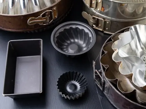 Collection de moules à gâteaux de différents types, certains en métal argenté, d'autres en métal noir, prêts pour la pâtisserie.