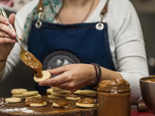 Une main dépose une cuillère de dulce de leche sur un biscuit rond, préparant des **caras crakine fait maison**.
