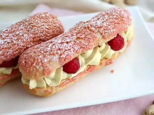 Deux éclairs à la framboise, garnis de crème légère et de fruits rouges, saupoudrés de sucre glace.