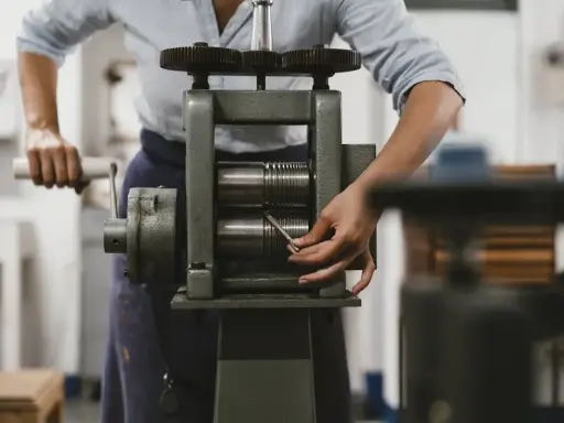 Une personne utilise un laminoir manuel pour travailler le métal. Les rouleaux sont prêts à aplatir un fil.