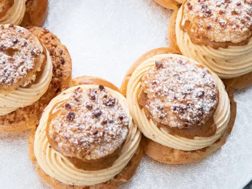 Plusieurs Paris-Brest, des pâtisseries rondes à la pâte à choux garnies de crème onctueuse et saupoudrées de sucre glace et d'amandes.