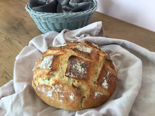 Un pain artisanal doré, prêt à être dégusté après son temps de pousse. Une corbeille de serviettes grises est visible en arrière-plan.