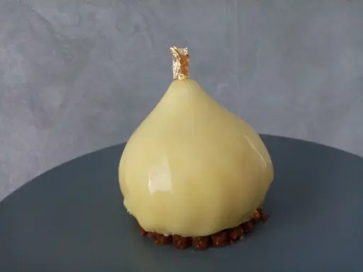 Délice en forme de poire, recouvert d'un glacage miroir jaune éclatant, sur un lit de crumble croquant, orné d'une touche de feuille d'or.