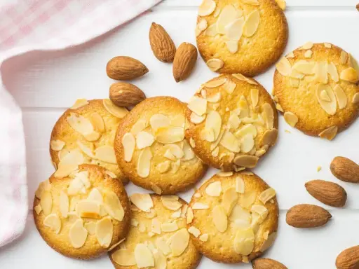 Des biscuits moelleux aux amandes, parsemés d'éclats d'amandes, sur un fond blanc avec une serviette à carreaux roses.