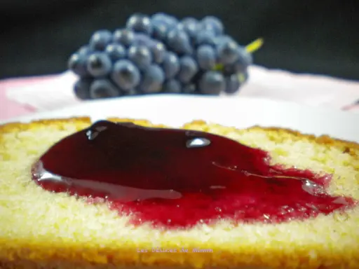 Tranche de gâteau moelleux nappée d'une généreuse gelée de raisin, avec une grappe de raisins bleus en arrière-plan.