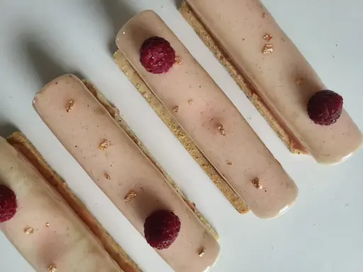 Quatre délicieux rectangles de crème chiboust ou diplomate, ornés de framboises fraîches et de feuilles d'or comestibles.